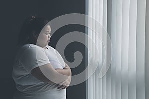 Lonely obese woman standing near the window