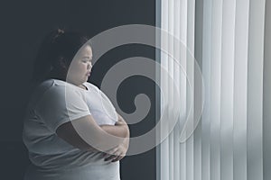 Lonely obese woman standing near the window photo