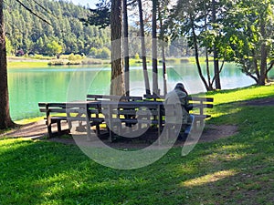 A lonely old man sits on a bench near lake in Coredo and Tavon