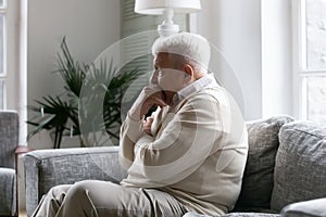 Lonely old man sitting on couch lost in pessimistic thoughts