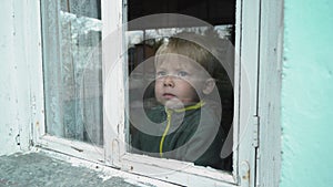 A lonely orphan boy looks through an old window.