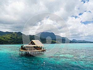 Lonely overwater bungalow of black pearl farmers. Blue azure turquoise lagoon. Raiatea island, French Polynesia. Aerial view.