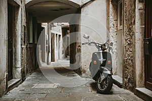 Lonely parked retro scooter in front of one house in old empty narrow alley with stone road of historic town of Piran in Slovenia