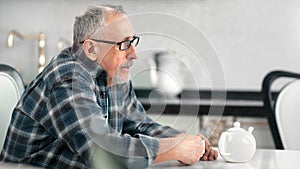 Lonely pensive aging male drinking tea at white kitchen having calmness emotion medium close-up