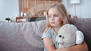 Lonely pensive little girl hugging bear toy feeling love best friend sitting couch waiting parents