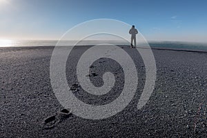 Lonely person silhouette standing far in background and footprints on the sand