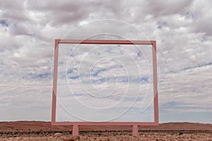 A lonely pink arch stands in the Namib desert against the backdrop of a cloudy sky