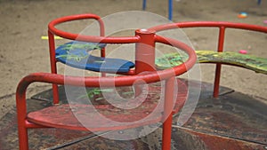 Lonely red empty deserted swing in an old abandoned amusement park. Swinging seat moving back and forth. Carousel