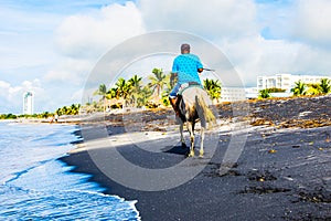 A lonely rider on a white horse slowly moving along a Panama beach