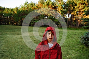 A lonely sad boy in a red windbreaker against the backdrop of a forest or park.