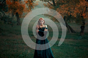 Lonely sad girl walks alone in terrible dark dangerous forest in long green emerald dress and raincoat with open