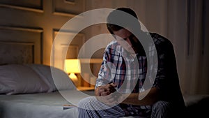 Lonely sad man sitting on bed, experiencing painful wife loss, grief and sorrow