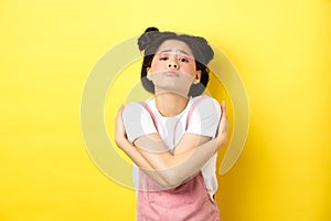 Lonely sad teen girl hugging herself, wanting to relationship and cuddles, standing alone on yellow background