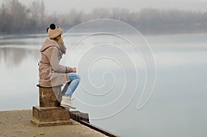 Lonely sad teenage girl sitting on dock on cold winter day