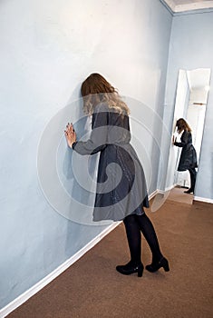 Lonely, sad young girl rests against a wall with a reflection in the mirror. The concept of domestic violence, abuse and