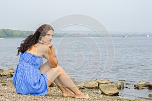 Lonely sad young girl sitting on river bank