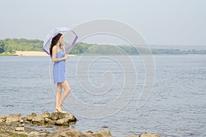 Lonely sad young girl with an umbrella stands on the bank of the river and looks into the distance