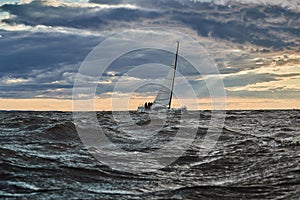 The lonely sailboat on the horizon in sea at sunset, the storm sky of different colors, big waves, sail regatta, cloudy