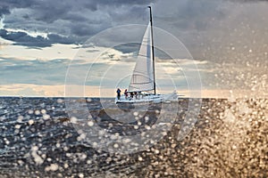 The lonely sailboat on the horizon through splashes of sea at sunset, the storm sky of different colors, big waves, sail