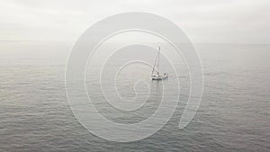 Lonely sailboat lowered sails sailing in sea and overcast sky on background