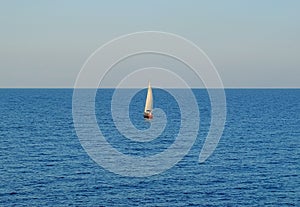 Lonely sailboat in the sea under blue sky. Lonely sailing vessel on blue water