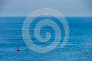 A lonely sailing boat crossing a blue, calm ocean near Mons Klint as the equipage enjoys a relaxing escape away in the Baltic sea