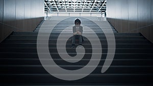 Lonely schoolchild sitting alone on school staircase closeup. Boy hide in hall.