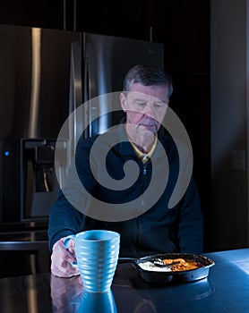 Lonely senior man eating ready meal at table
