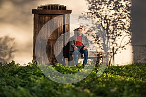 Lonely senior man sitting on bench in front of old house, eyes closed.