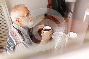 Lonely senior man sitting at kitchen table drinking tea