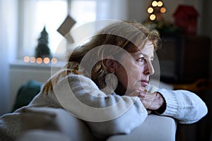 Lonely senior woman sitting on sofa indoors at Christmas, solitude concept.