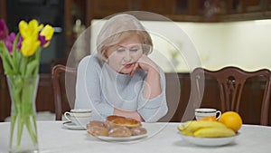 Lonely senior woman sitting at table sighing waiting for children. Portrait of hopeless sad Caucasian beautiful retiree