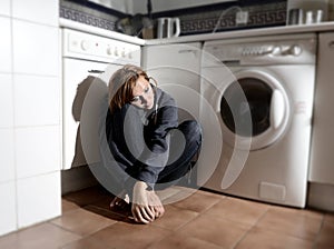 Lonely and sick woman sitting on kitchen floor in stress depression and sadness