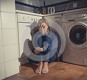 Lonely and sick woman sitting on kitchen floor in stress depression and sadness