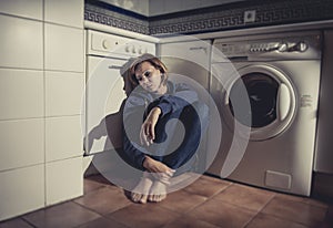 Lonely and sick woman sitting on kitchen floor in stress depression and sadness