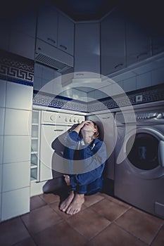 Lonely and sick woman sitting on kitchen floor in stress depression and sadness