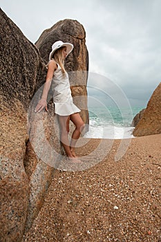 Lonely slender woman on a deserted beach on the background of large stones and a dark cloudy sky.