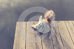 Lonely small girl sitting near river. Riskily situation