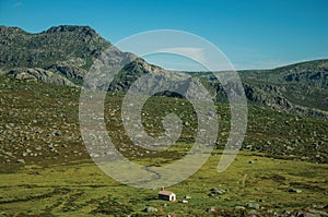 Lonely small house on green fields and rocky landscape