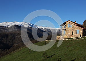 Lonely stone house on the hill on the background of snowy mountains, clear blue sky, horizontal