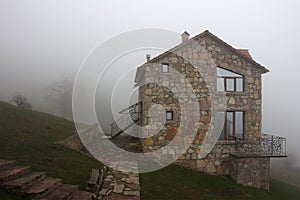 Lonely stone house on the hill in fog, side view