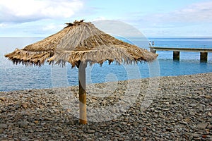 Lonely sunshade at wild beach and two silhouettes far away