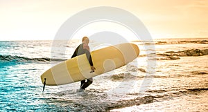 Lonely surfer walking with longboard at sunset in Tenerife - Surfing adventure lifestyle and sport travel concept