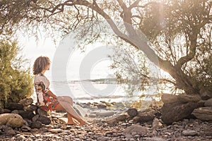 Lonely sweet beautiful middle age young woman sitting on the shore on a rock near the ocean. wave in background and peaceful place