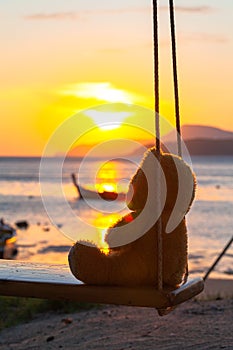 Lonely Teddy Bear sitting on a swing in front Rawai beach