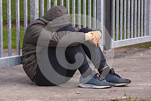 Lonely teenager sitting alone outside a metal fence with iron bars. Loneliness and bullying concep