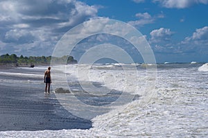 Lonely teenager standing on the beach near a large stone boulder during a storm