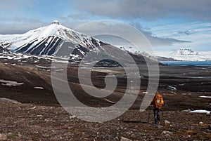 Lonely tourist hiking towards snow capped mountain in the Russian ghost town Pyramiden in Svalbard archipelago