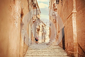 Lonely tourist walking on narrow streets with the old stone houses. Traveling around Malta island