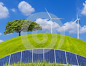 Lonely tree with photovoltaics solar panels and wind turbines generating electricity on green field and blue sky